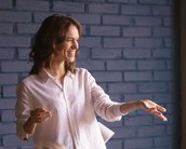 Eine Frau in einem weißen Hemd spricht und gestikuliert vor einem Publikum, das ihr aufmerksam zuhört. Im Hintergrund sind eine blaue Wand und ein Tisch mit Notizmaterialien sichtbar.